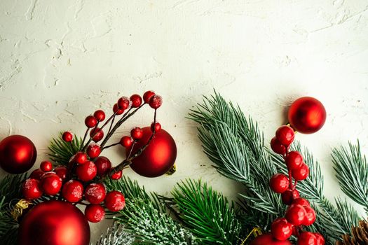 Christmas card concept with frame made with green fir branches, red decoration balls and berries on concrete background