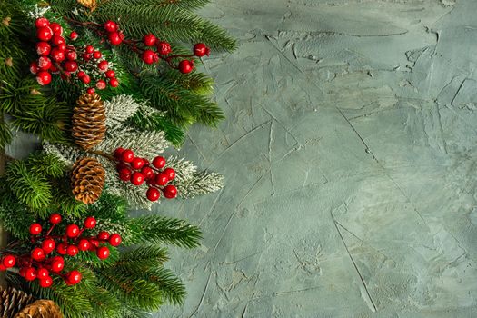 Christmas card concept with frame made with green fir branches, red decoration balls and berries on concrete background
