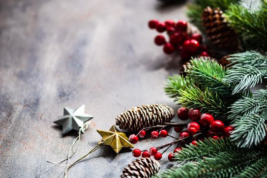 Christmas card concept with frame made with green fir branches, red decoration balls and berries on concrete background