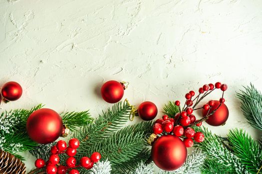 Christmas card concept with frame made with green fir branches, red decoration balls and berries on concrete background