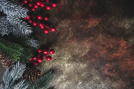Christmas card concept with frame made with green fir branches, red decoration balls and berries on concrete background