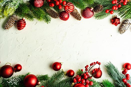 Christmas card concept with frame made with green fir branches, red decoration balls and berries on concrete background