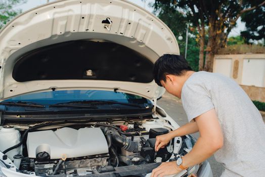 young stressed man having trouble with his broken car looking in frustration at failed engine