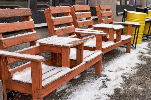 A wooden bench with tables for visitors to the cafe stands on the street and is covered with snow