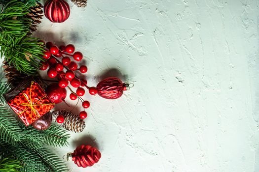 Christmas card concept with frame made with green fir branches, red decoration balls and berries on concrete background