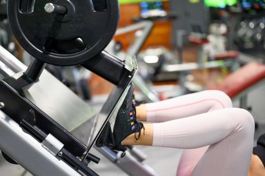 Side view of fit young sportswoman flexing her leg's muscles on exercise machine at the gym. High quality photo.