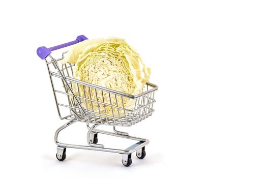 Green cabbage lies in a small supermarket trolley on a white background, close up