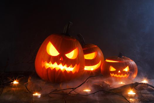 Halloween pumpkins head jack o lantern, candles and dry maple leaves in mist