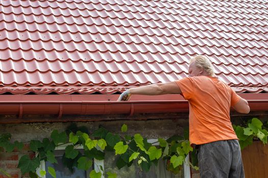 A man cleans out debris and leaves from the gutter system on the roof of his house.