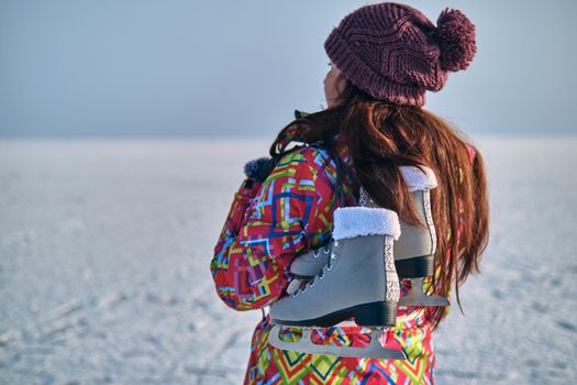 A woman in a ski suit holds skates on her shoulder and looks into the distance, after skiing on a frozen lake