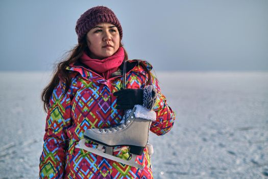 A woman in a ski suit holds skates on her shoulder and looks into the distance, after skiing on a frozen lake