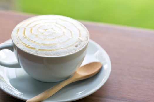 A cup of coffee on wooden table and green grass background.