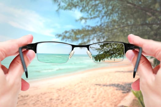 Female hand holding glasses focus mirror lens on sand sea travel trip.
