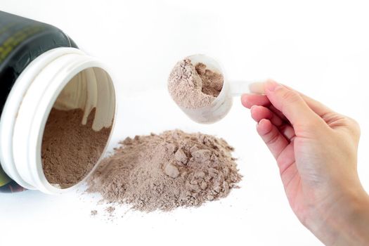 The hand raise a spoon measure Whey protein chocolate powder for fitness and bodybuilding gaining muscle.