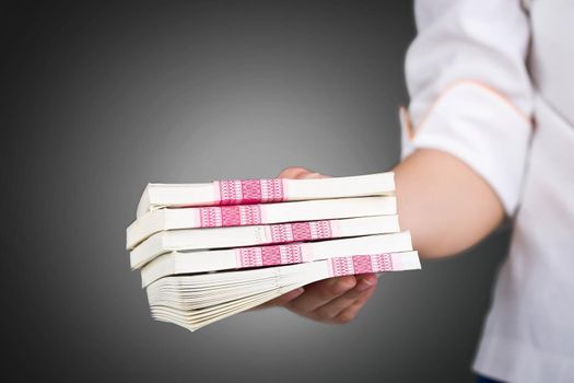 Female hand giving money pack on black background.