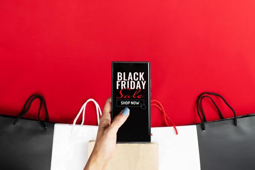 black friday sale, woman hand online shopping on smartphone with shopping bag on red background