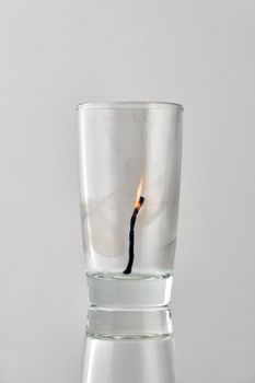 Remains of a dying match in a transparent glass on a light background. Concept, symbol