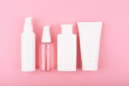 Trendy modern minimal flat lay with a set of beauty products in white tubes in a row against pink background. Concept of daily skin care routine