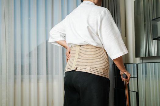 Senior back pain woman with walking stick at home