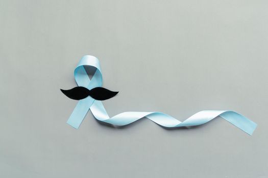 November light blue ribbon with mustache on gray background with copy space, Prostate cancer awareness month, men's health concept