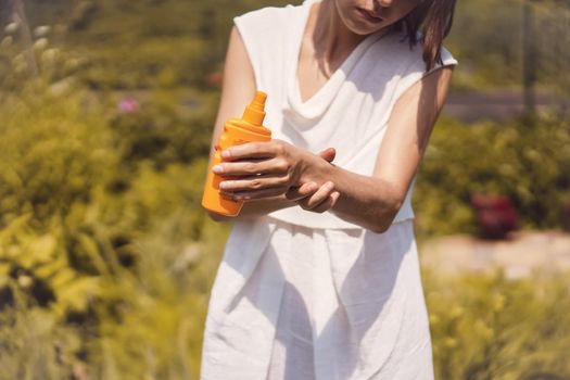 A young girl in a white summer dress applies sunscreen gel to her arms and shoulders, a woman takes care of her skin on a sunny day.