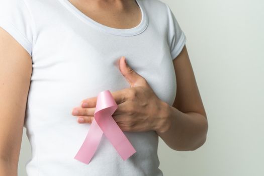 pink badge ribbon on woman hand touching chest to support breast cancer cause. breast cancer awareness concept