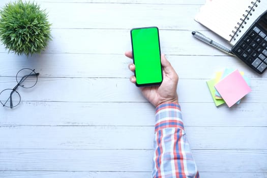 Top view of man hand holding smart phone with empty screen on office desk .