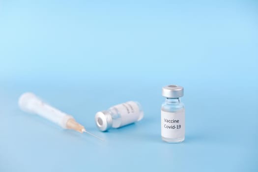 Close up of coronavirus vaccine and syringe on blue background.
