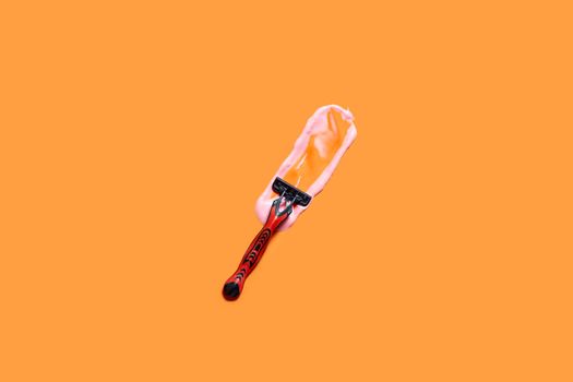 Shaving foam gel and razor on orange background. A multiple use shaving razor and cream. View from above