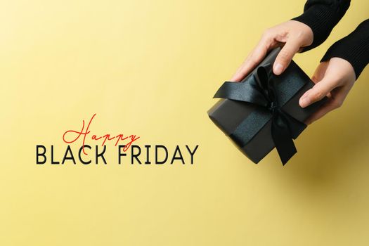 black friday sale, woman hand give the gift box on yellow background