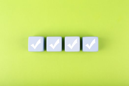 Four checkmarks on white cubes against bright green background. Concept of questionary, checklist, to do list, planning, business or verification. Creative minimal composition