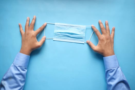 man hand holding surgical face mask on blue background