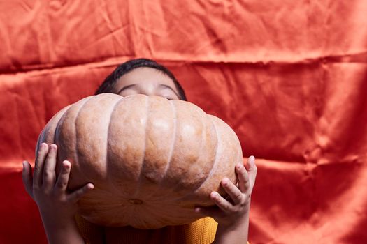 A boy holding a big pumpkin over orange background