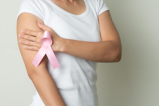 pink badge ribbon on woman hand touching chest to support breast cancer cause. breast cancer awareness concept