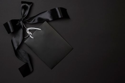 Black friday concept. Black shopping bag on cloth holder with big black ribbon on dark background