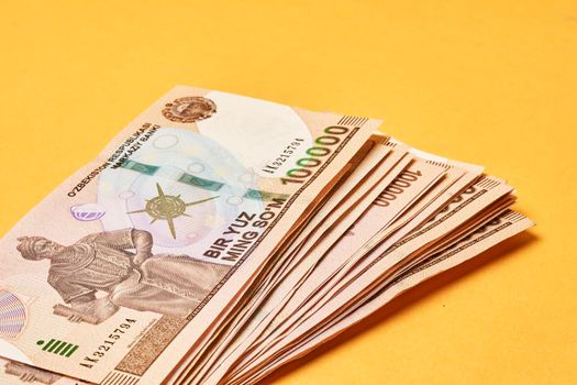 Pile of Uzbek sums on yellow. Uzbek currency money bill. A stack of one hundred thousand Uzbek sum. Uzbek money. 100000 sum