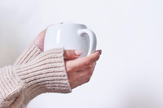 Female hand holding hot tea cup against white background. A woman in warm knitted sweater holds in hands tasty herbal tea