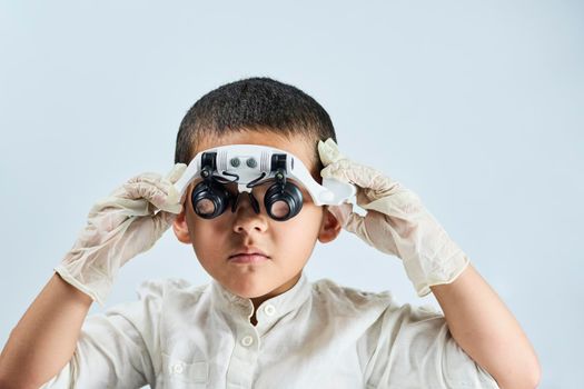 A multiethnic boy in magnifying eyeglasses against the white table