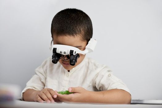 A little smart boy discovering the micro world with headband magnifying glass