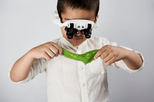 Schoolboy equipped with headband magnifying glass conducting scientific experiments at the workshop