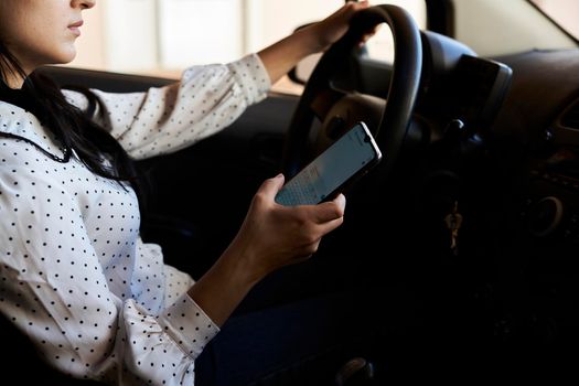 Young multiracial woman texting and driving car. Woman using cellphone while driving car. Female using smartphone while travelling by car. Driving while holding cell phone