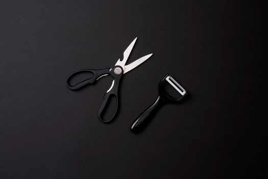 Kitchen utensils on black. Kitchen scissors and peeler or slicer on black background