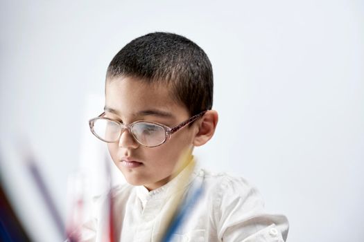 Portrait of a schoolboy in white fully concentrated on his homework
