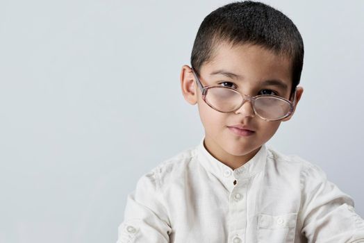 Portrait of 7 years old mixed race boy looking at the camera. A smart schoolboy portrait against the white background