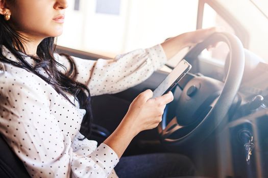 Young multiracial woman texting and driving car. Woman using cellphone while driving car. Female using smartphone while travelling by car. Driving while holding cell phone