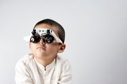 Studio portrait of little scientist in special magnifying headset glasses with copy space