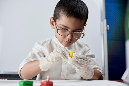 A portrait of cute boy in protective gloves and glasses making plasticine figures on the table