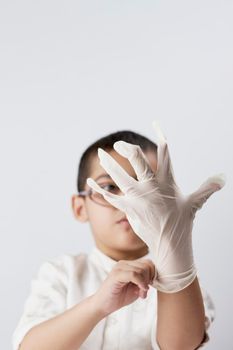 A small 7 years old boy in glasses wears latex protective gloves