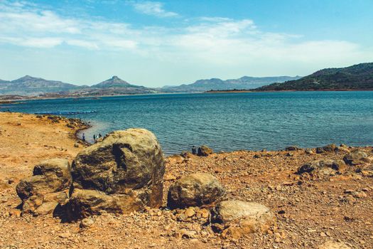 landscape of a lake from its rocky shore with mountains in the background