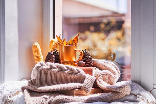 Corns, autumn leaves, pine cones and coffee cup on windowsill. Creative autumnal background near the windows in a sunny autumn day